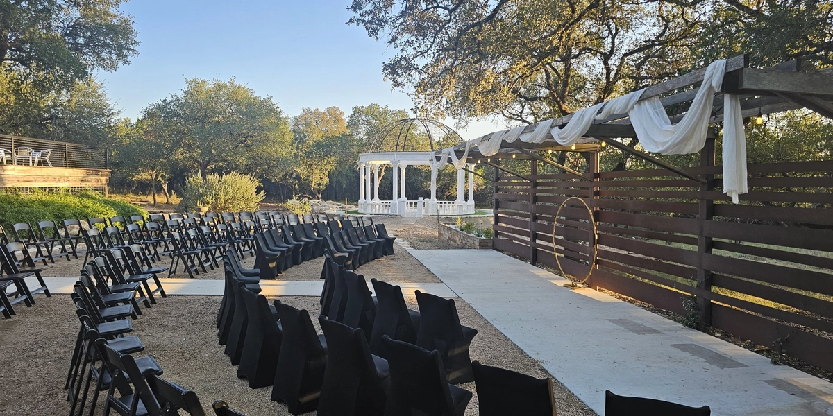 Outdoor ceremony site with a draped wooden pergola and the marble dome beyond at Prima Vista in Wimberley, Texas