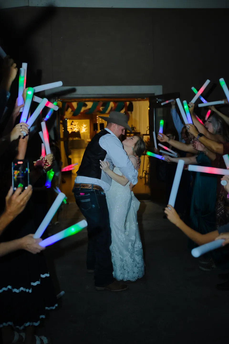 Newlyweds kissing under a tunnel of glow sticks at their send-off from the Kosciusko Community Hall in Kosciusko, Texas