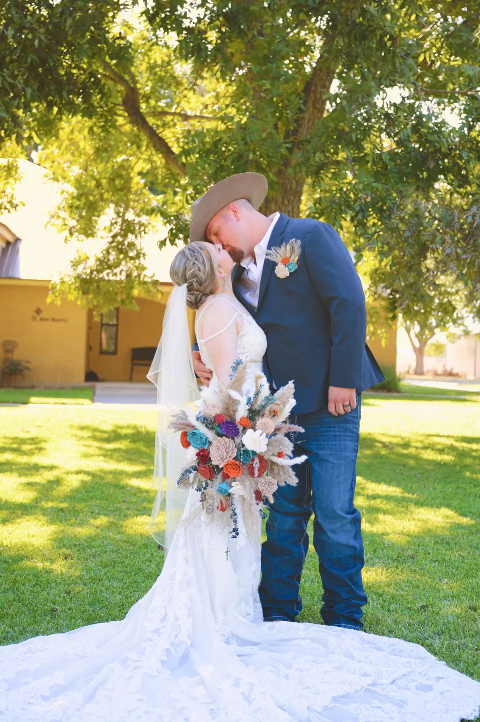 Couple kissing in the sunlight with a dried-flower bouquet and cathedral-length lace train in Kosciusko, Texas
