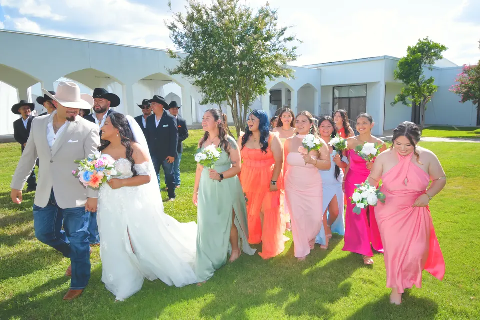 Couple walking across the lawn with their bridesmaids in rainbow dresses at their San Antonio wedding