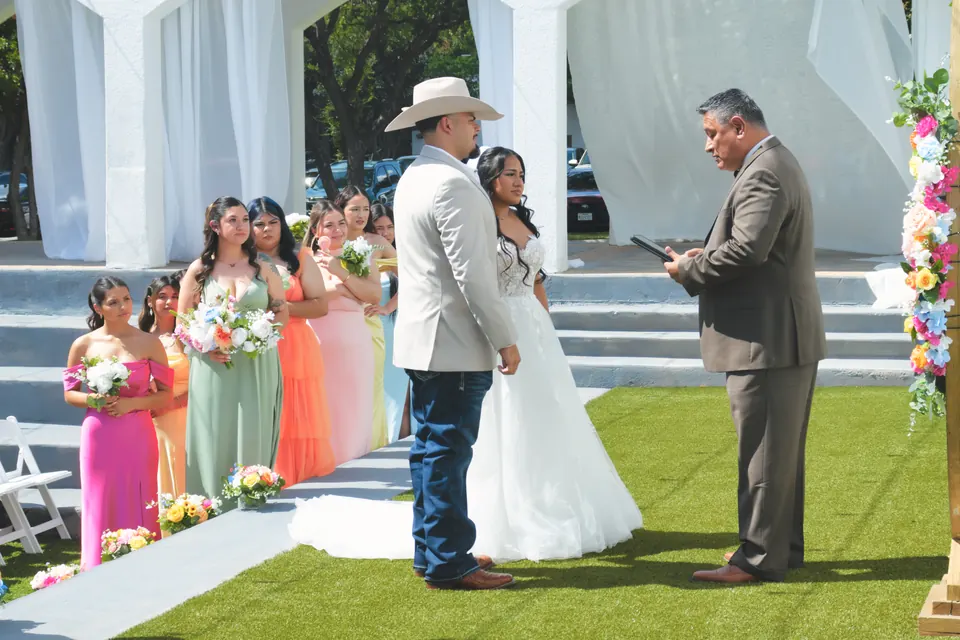Couple exchanging vows under a gold floral arch with bridesmaids in bright gowns at the Phoenician Ballroom Event Center in San Antonio