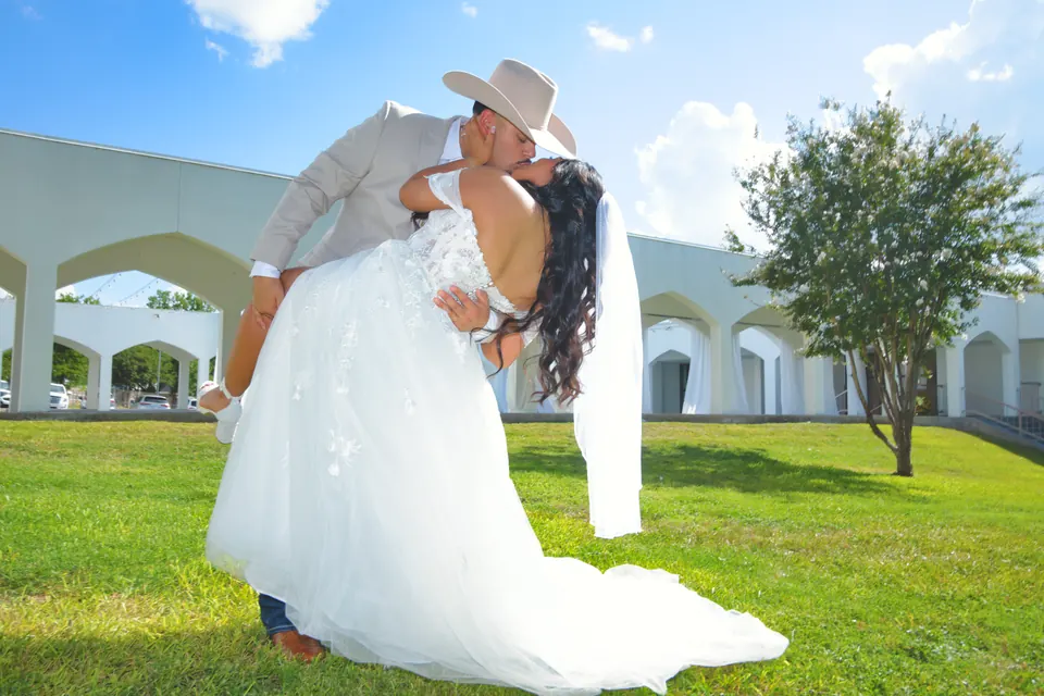 Groom in a cowboy hat dipping the bride under a blue sky in San Antonio