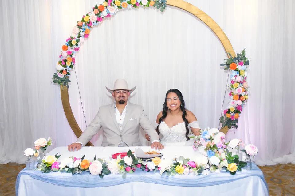 Newlyweds at their sweetheart table beneath a gold floral arch at the Phoenician Ballroom Event Center in San Antonio