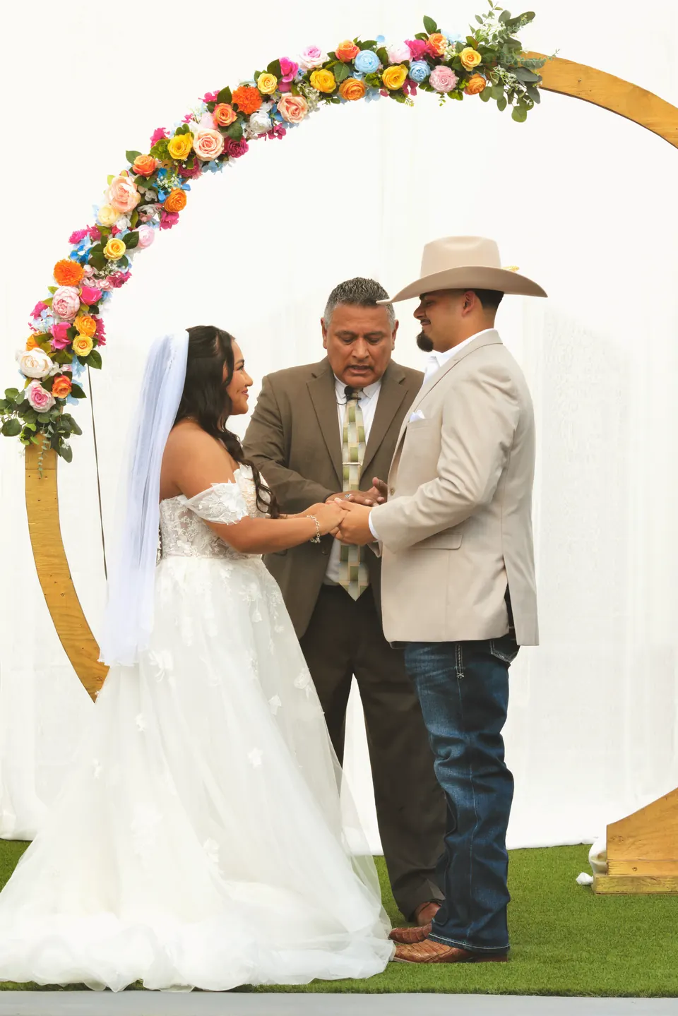 Bride and groom holding hands during their vows under a colorful floral arch in San Antonio