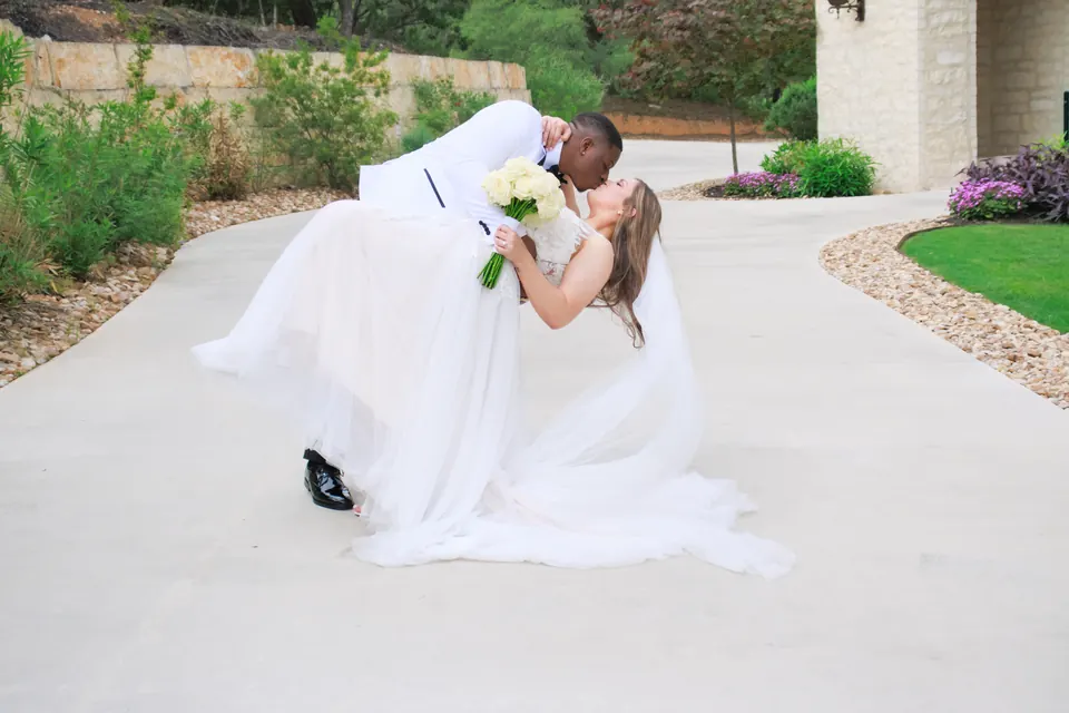 Groom in a white tuxedo dipping the bride on the stone drive at The Preserve at Canyon Lake
