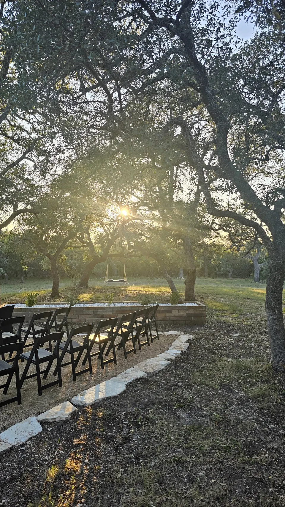 Golden-hour sun through live oaks beside a row of chairs at Prima Vista in Wimberley, Texas