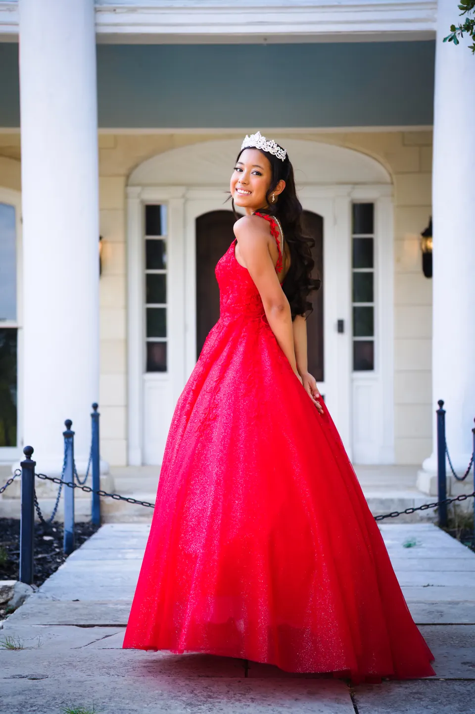 Retrato de cuerpo completo de la quinceañera con su vestido rojo frente a una puerta blanca en Denman Estate Park, San Antonio