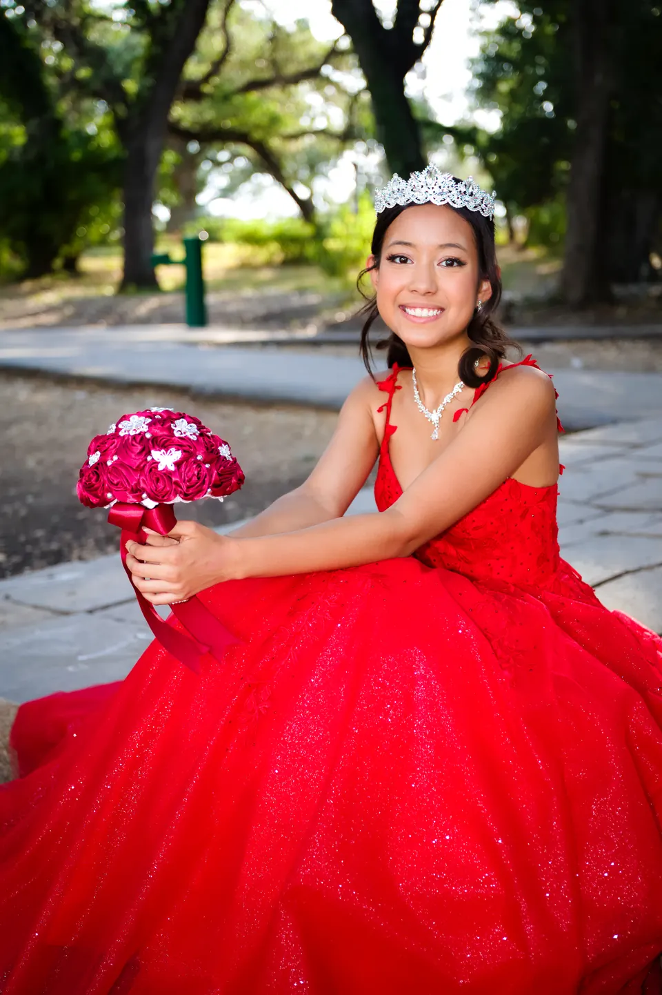 Quinceañera laughing while holding a red rose bouquet in her pre-quince portraits at Denman Estate Park in San Antonio