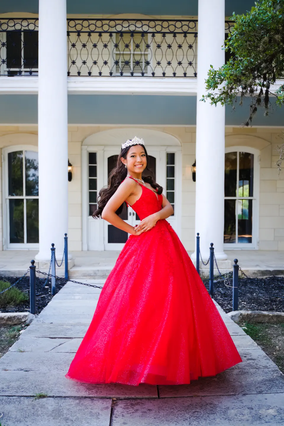 Quinceañera moviendo la falda de su vestido rojo frente a la mansión en Denman Estate Park, San Antonio
