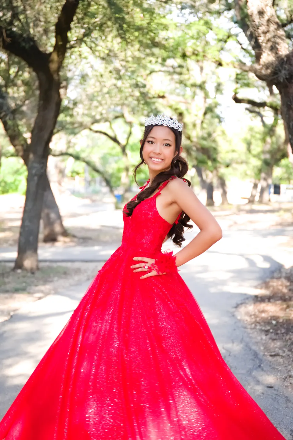 Quinceañera with a hand on her hip under shady oak trees at Denman Estate Park in San Antonio