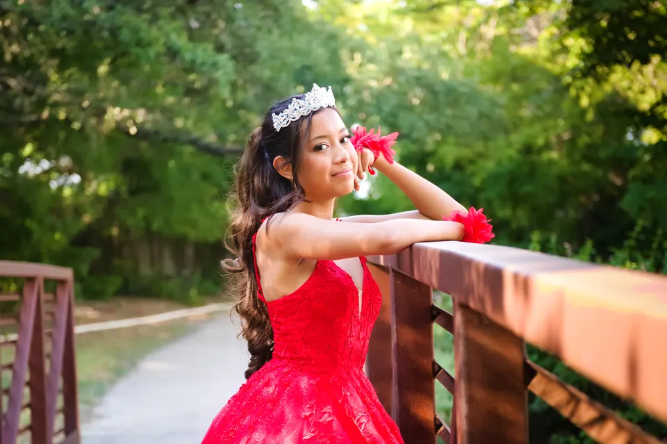 Quinceañera sonriendo recargada en el barandal de un puente de madera en Denman Estate Park, San Antonio