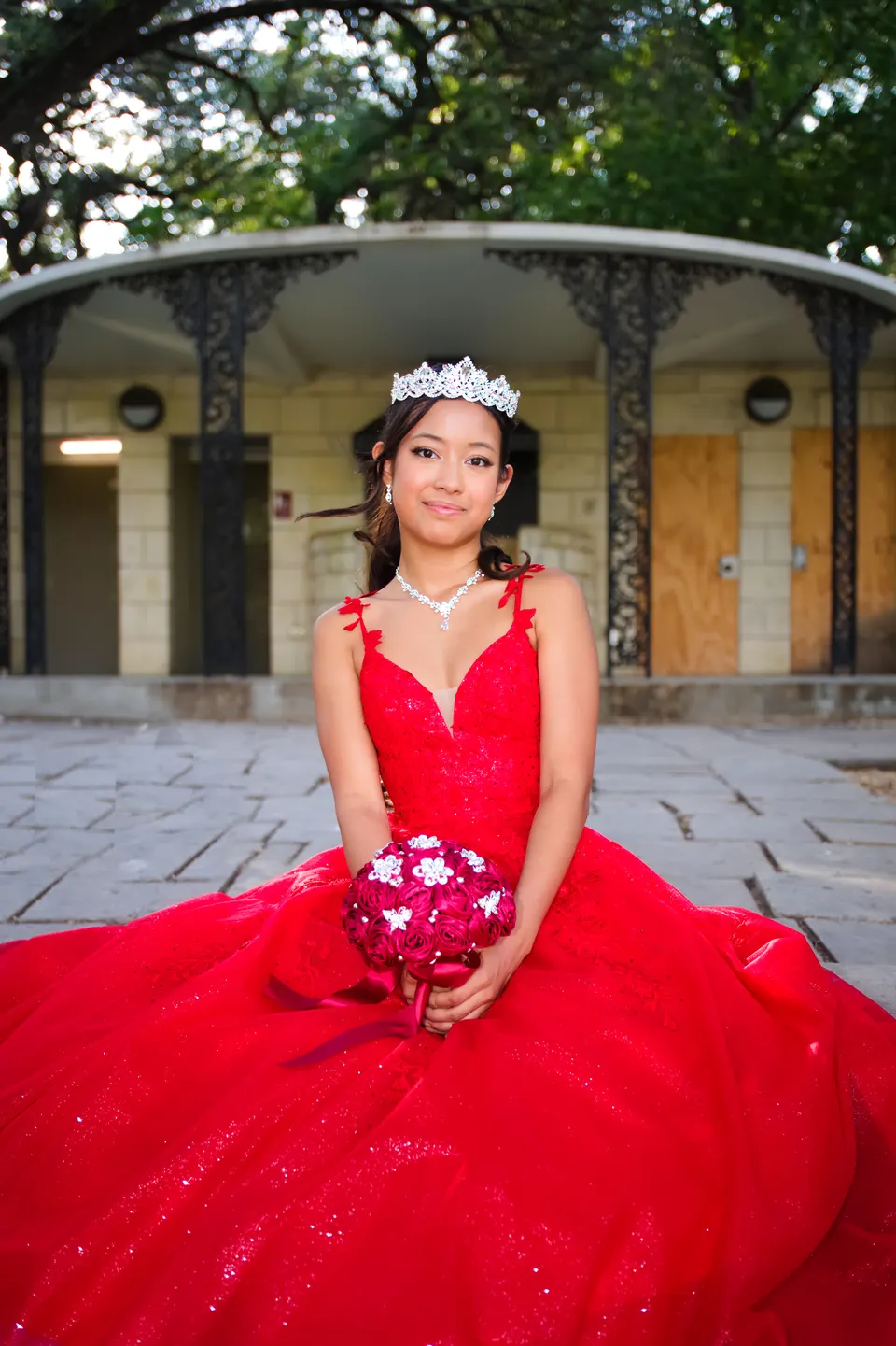 Quinceañera sentada con su ramo y la falda de su vestido extendida sobre el piso de piedra en Denman Estate Park, San Antonio