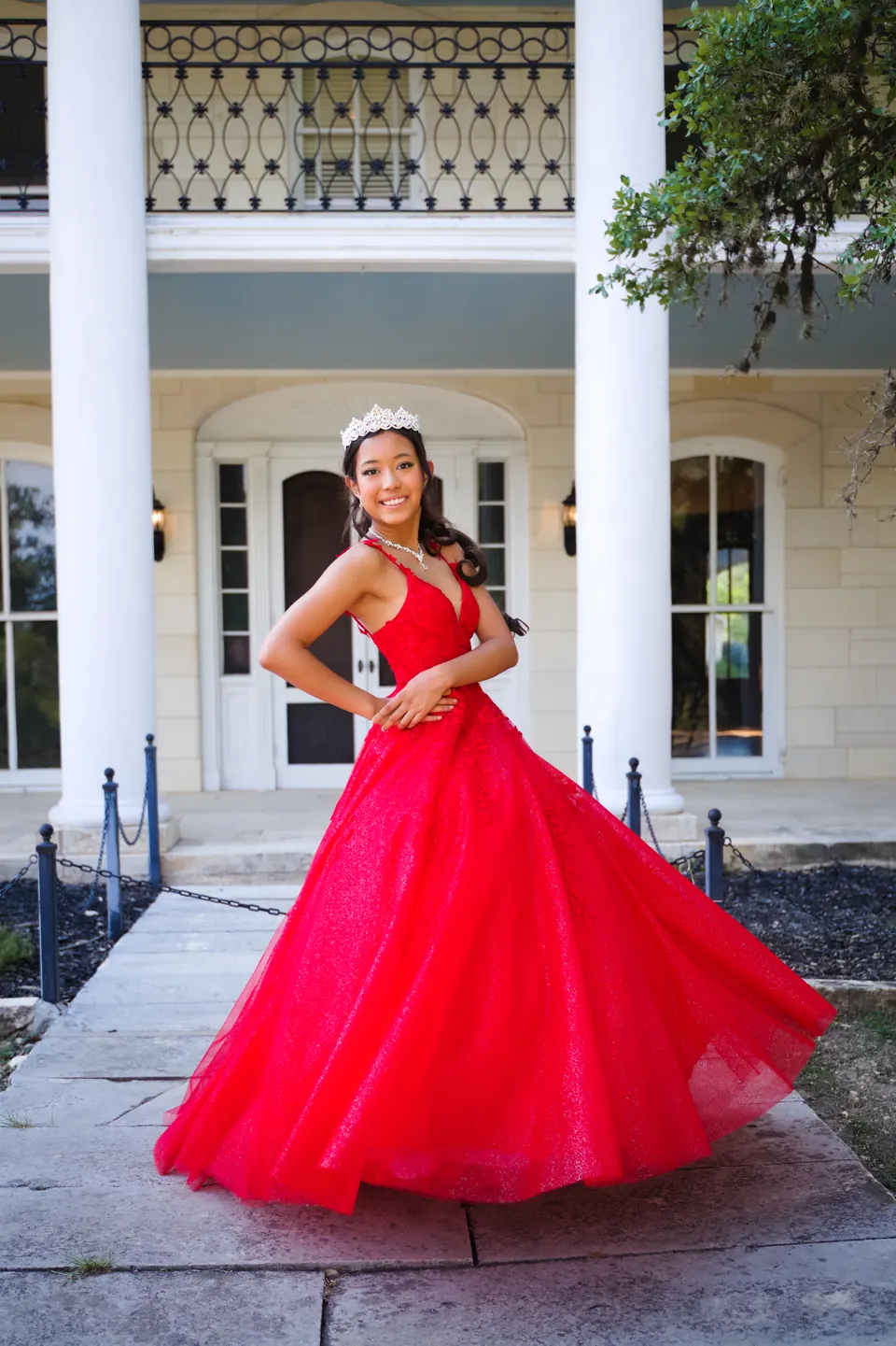 Quinceañera swishing her red ball gown in front of a white-columned mansion at Denman Estate Park in San Antonio