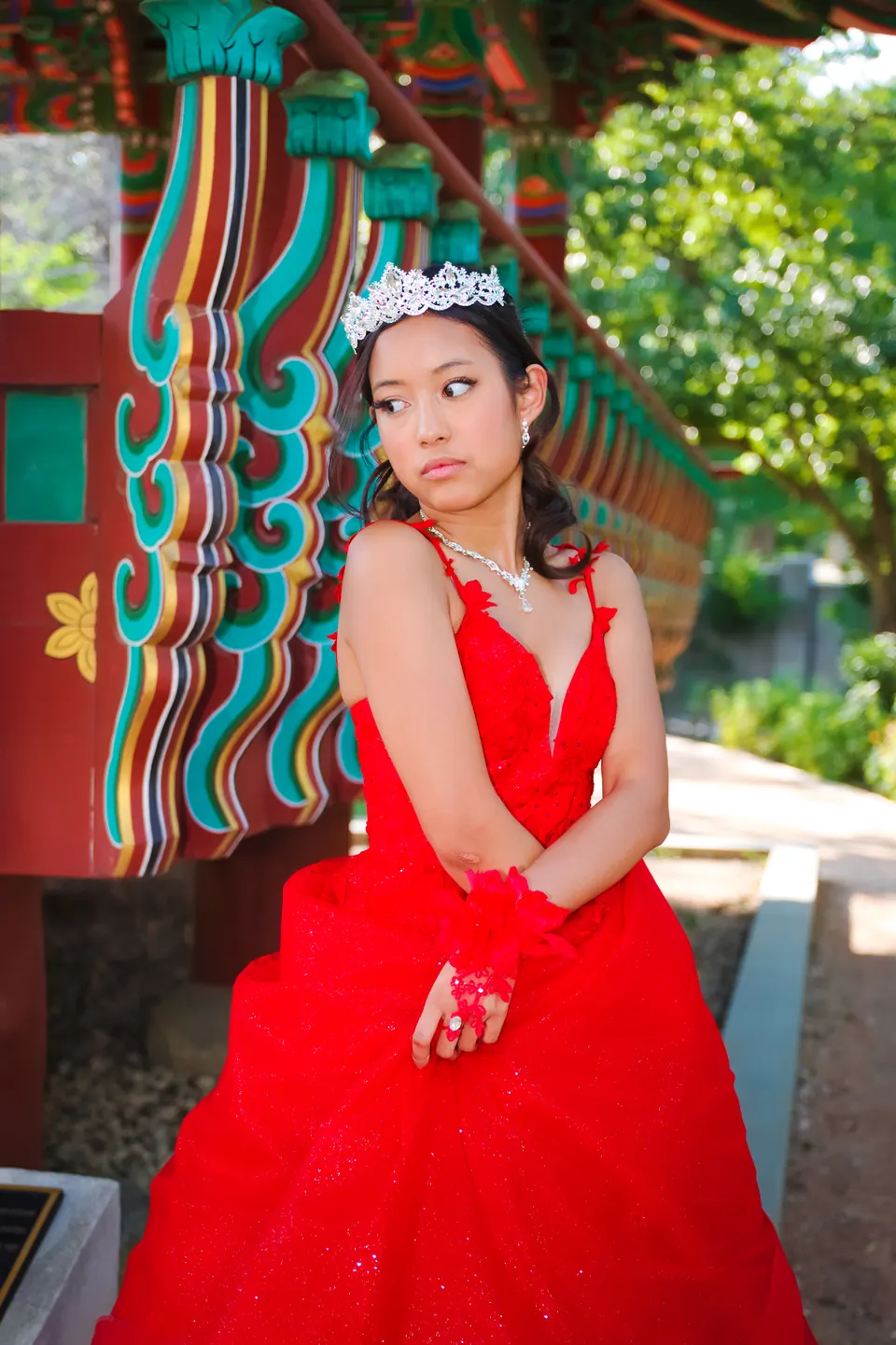 Quinceañera con mirada pensativa junto a las columnas pintadas del pabellón coreano en Denman Estate Park, San Antonio