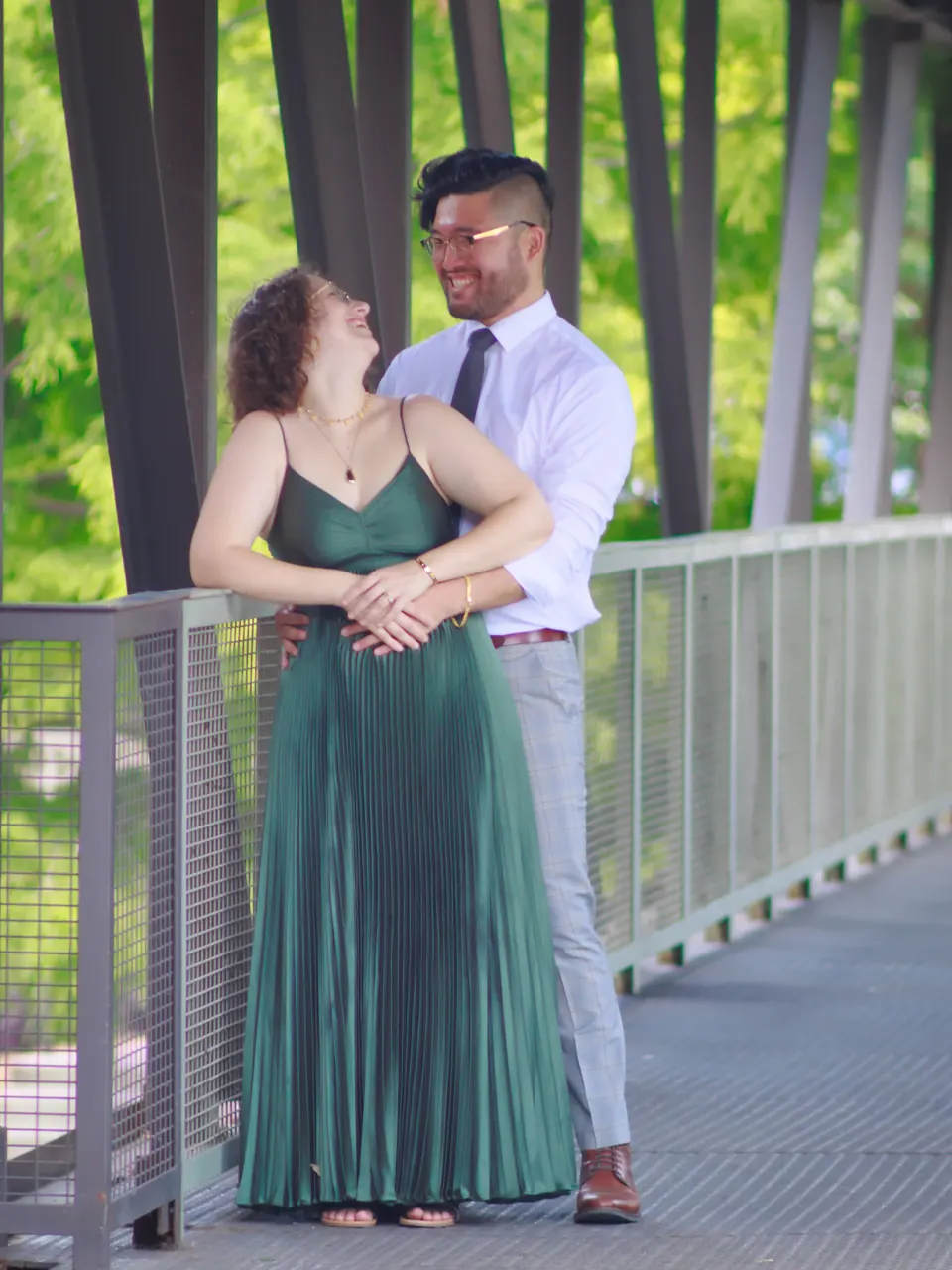 Engaged couple leaning on a bridge railing and smiling in San Antonio