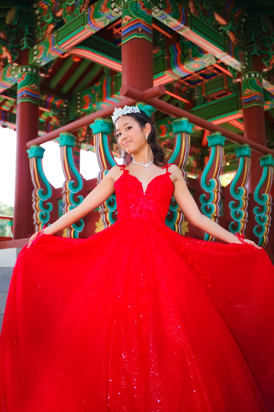 Quinceañera spreading her red ball gown in front of a colorful pavilion at Denman Estate Park in San Antonio