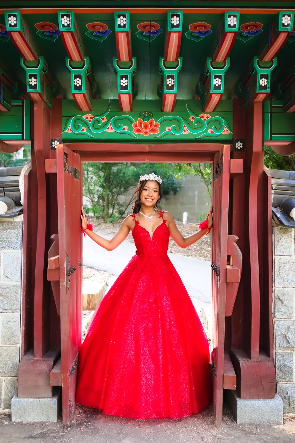 Quinceañera framed by a painted pavilion gate in her red gown during her portrait session at Denman Estate Park in San Antonio