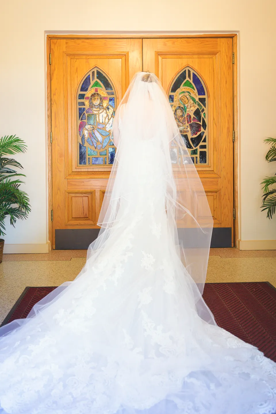 Bride's cathedral veil and lace train spread across the red carpet at the doors of St. Anne's Catholic Church in Kosciusko, Texas