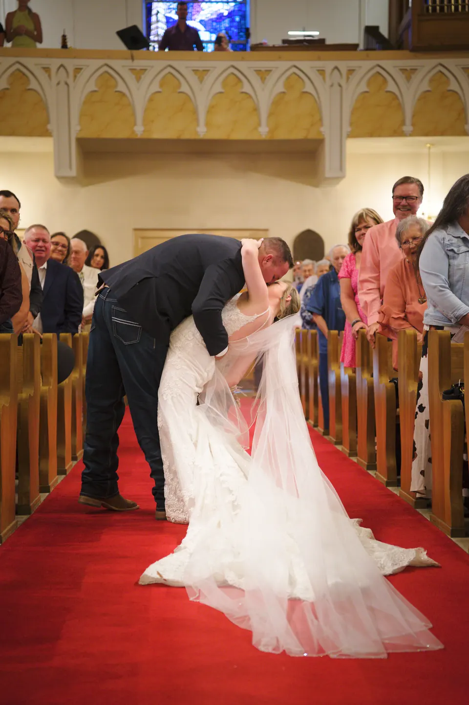 Groom dipping the bride for a kiss in the aisle of St. Anne's Catholic Church as guests cheer in Kosciusko, Texas