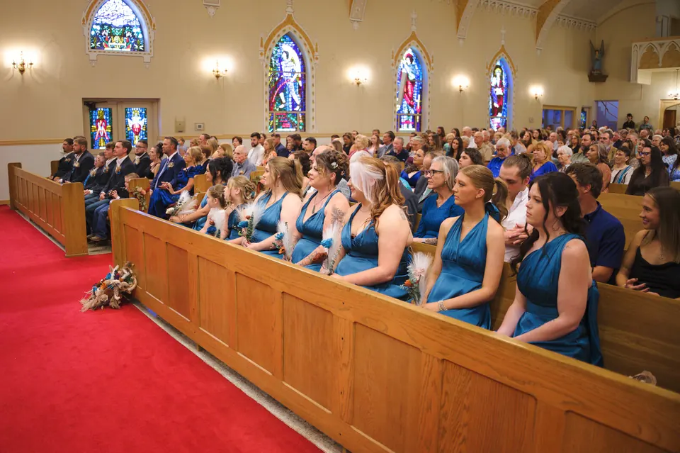 Bridesmaids in dusty blue seated in the front pew of St. Anne's Catholic Church in Kosciusko, Texas