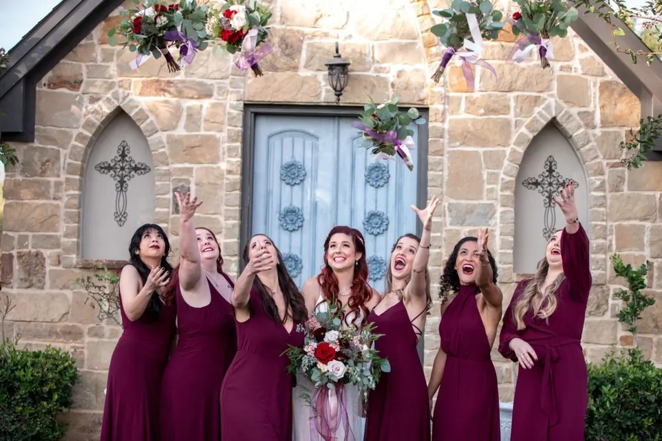 Bridesmaids in burgundy celebrating in front of the stone facade at Thistlewood Manor & Gardens